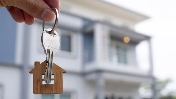 hand holding house key with house-shaped keychain and house in background